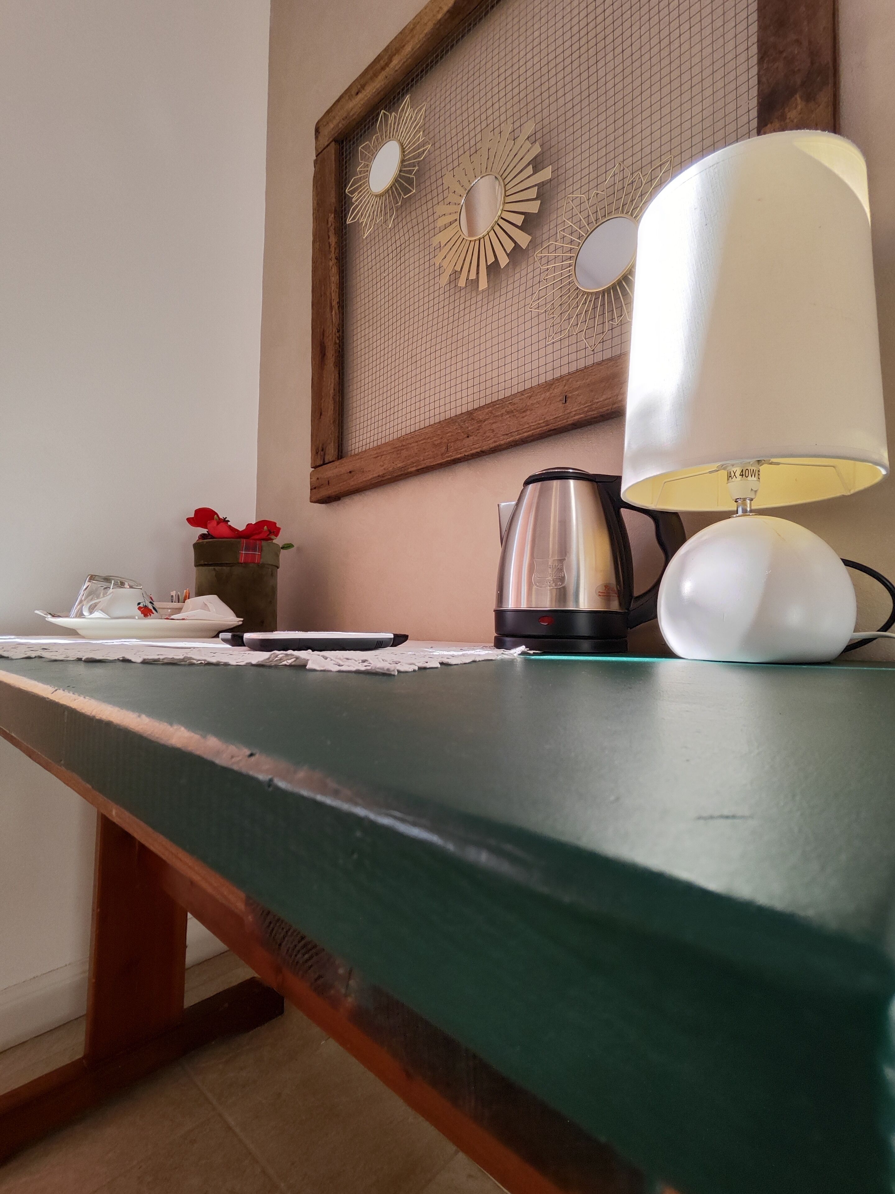 Ein Holztisch mit einer weißen Lampe, einem Wasserkocher und einem Teller mit einer roten Blume.
