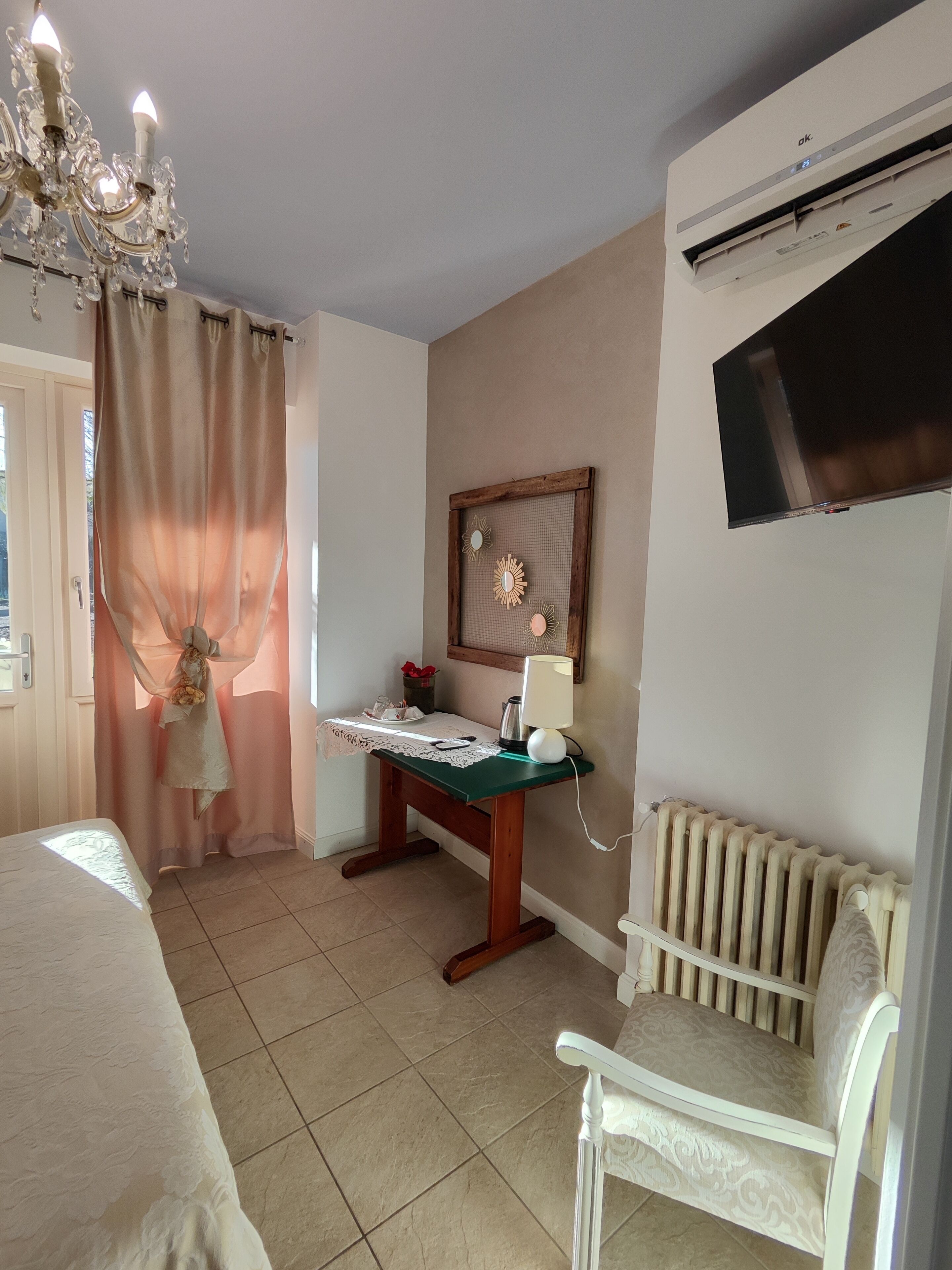 A bedroom with a bed, a desk with a lamp, a chair, a radiator, and a TV on the wall.