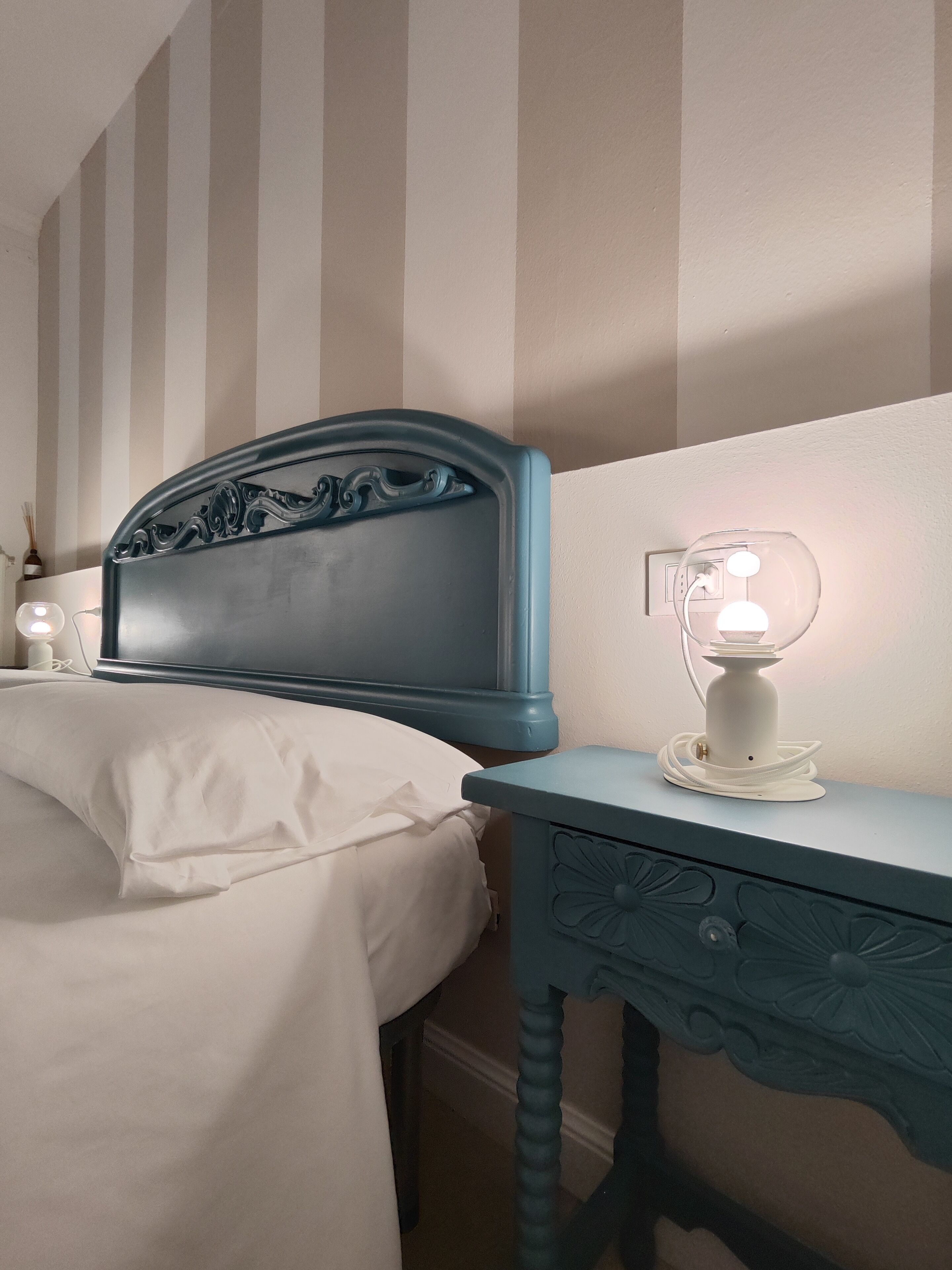 Une chambre à coucher avec un lit, une table de chevet avec une lampe et un mur à rayures verticales.