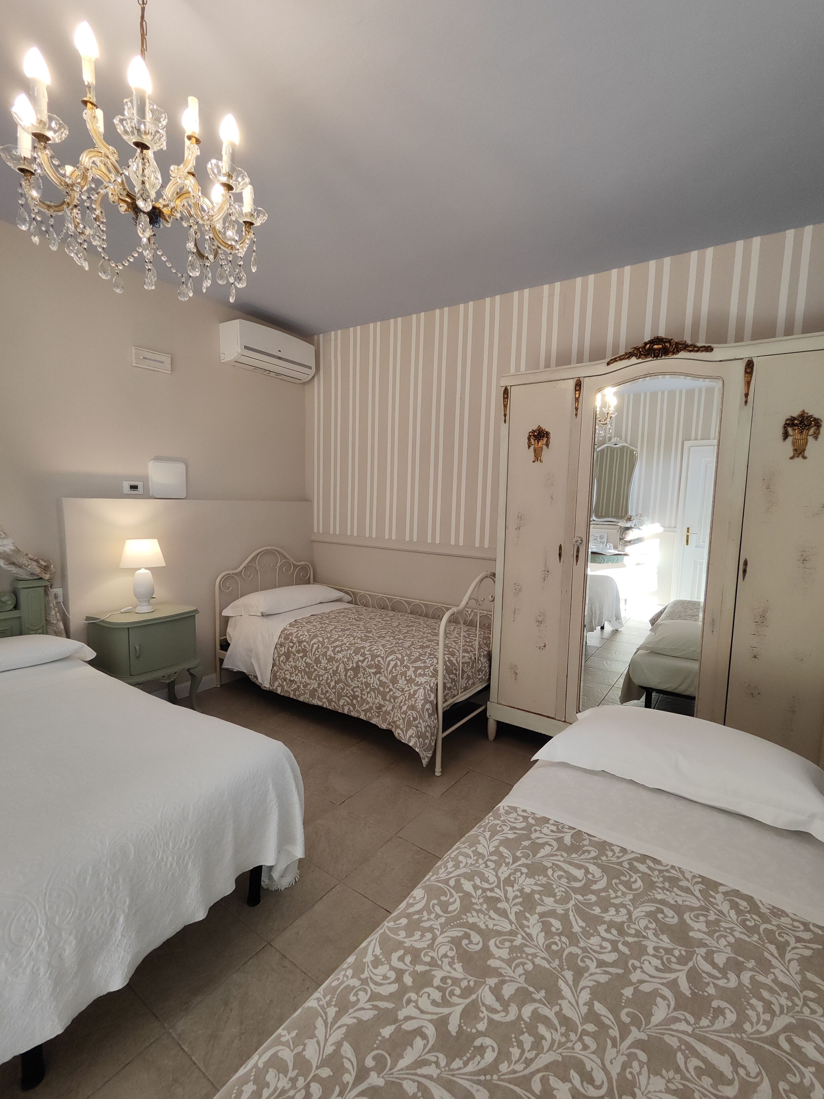Ein Schlafzimmer mit zwei Betten, einem Kronleuchter, einem Nachttisch mit Lampe, einem Kleiderschrank und einem Spiegel.