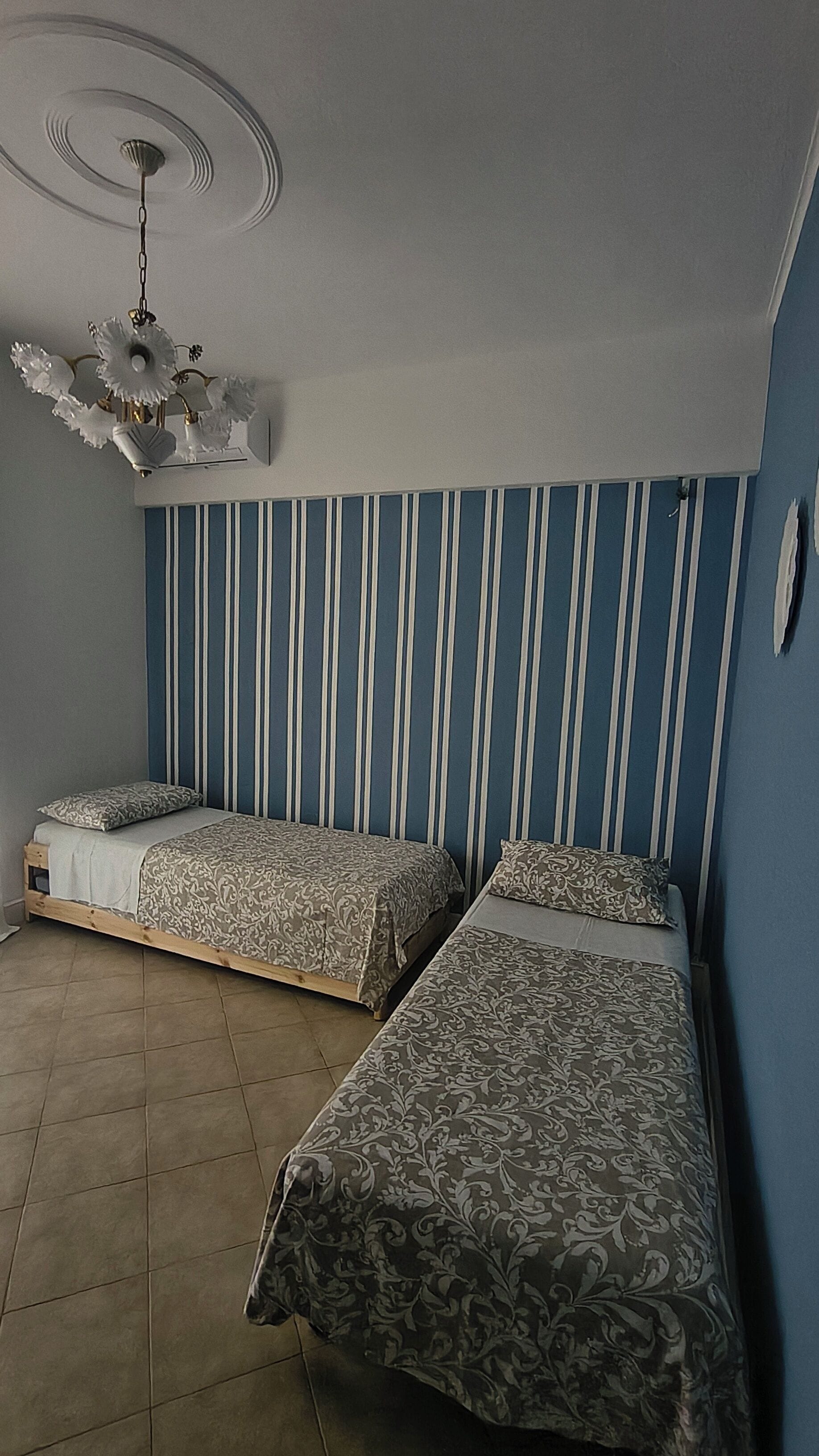 Une chambre avec deux lits, un ventilateur de plafond et un mur à rayures.