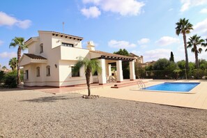 Una casa de dues plantes amb piscina, palmeres i una pèrgola.