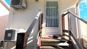 A wooden staircase leading to a door with a window, flanked by air conditioning units. - LE CLOS DE VAL - ACCOMMODATION - TERRACE SEA VIEW - HEATED SWIMMING POOL  (La Possession)