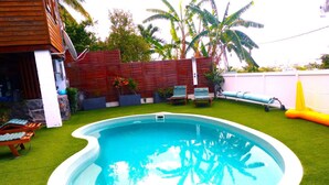 A swimming pool with artificial grass, lounge chairs, and a wooden deck. - LE CLOS DE VAL - ACCOMMODATION - TERRACE SEA VIEW - HEATED SWIMMING POOL  (La Possession)