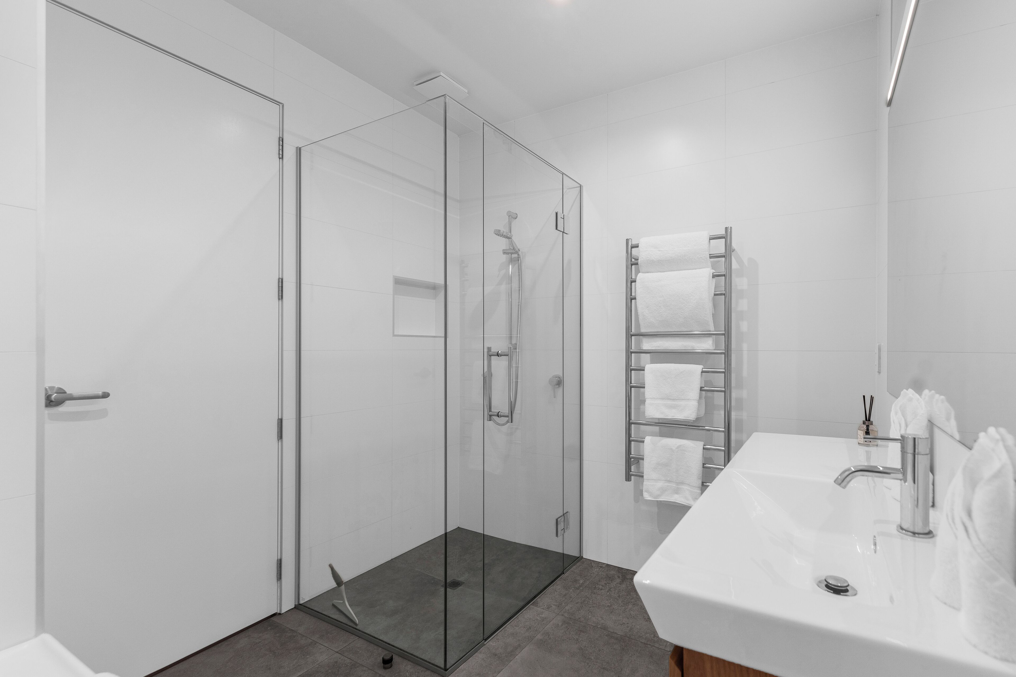Een moderne badkamer met een douchecabine van glas, een wit wastafelmeubel met spiegel en een handdoekhouder.