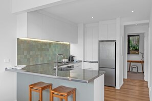 Een moderne keuken met een groot schiereiland, witte kastjes en een betegelde spatwand.