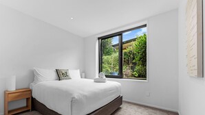 Une chambre avec une grande fenêtre, un lit, une table de chevet et un luminaire fixé au mur.