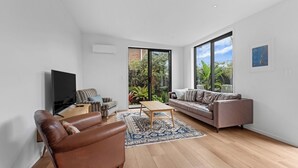 Un salon moderne doté d’un grand téléviseur, de deux canapés, d’une table basse et offrant une vue sur la verdure grâce à de grandes fenêtres.
