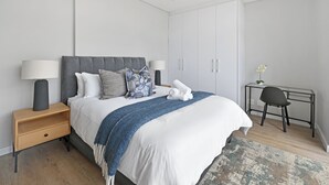 A modern bedroom with a bed, bedside tables, a desk, and a chair. - 2-Bed City Escape with Mountain Views (Cape Town)