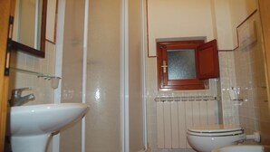 Un baño con lavamanos blanco, inodoro, cabina de ducha y espejo.