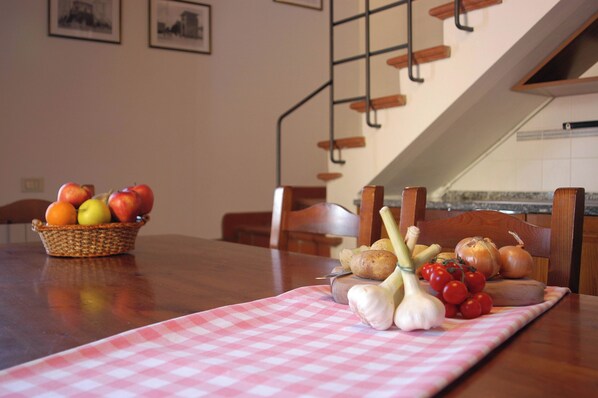 Una mesa de comedor con mantel a cuadros, una cesta de frutas y una tabla de madera con verduras.