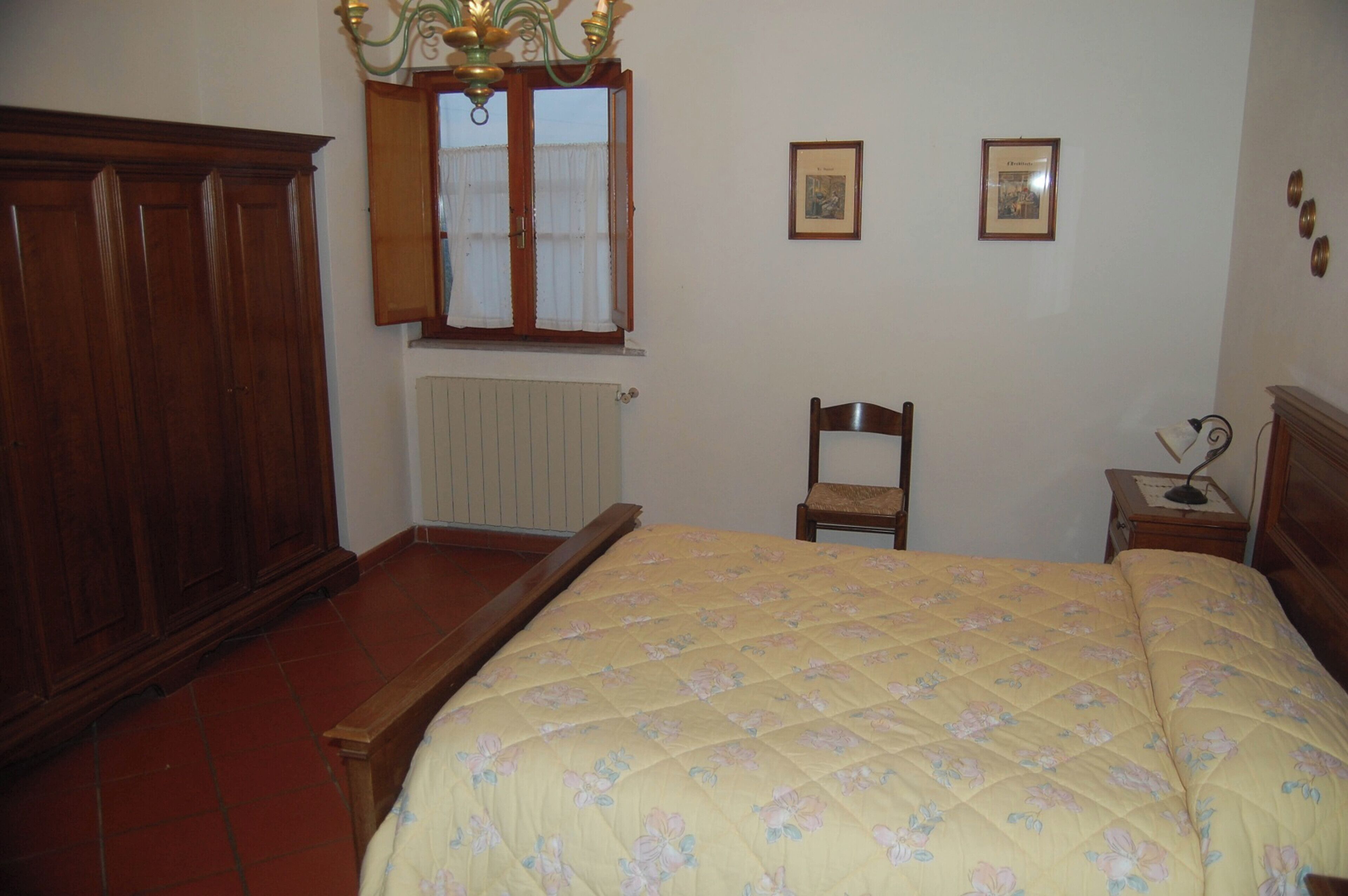 A bedroom with a bed, wooden wardrobe, chair, bedside table, and a window with curtains.