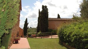 Un patio con un edificio de ladrillo, un sendero pavimentado y altos cipreses.