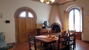 Un comedor con una mesa de madera, sillas y un televisor. Hay dos puertas y una chimenea.