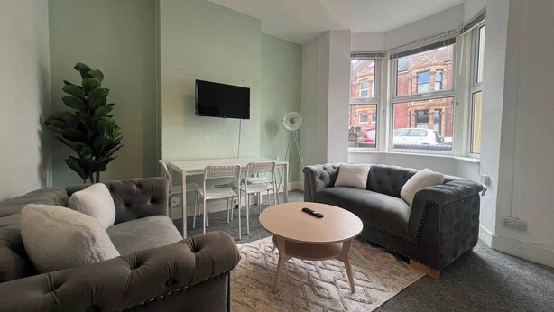 A living room with two grey sofas, a round coffee table, a TV on the wall, and a large window with a view of buildings.