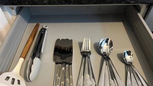 A drawer containing various kitchen utensils including a spatula, tongs, forks, spoons, and a ladle.