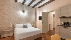 A bedroom with a bed, bedside tables, a nightstand, a wooden chair, a kitchen area with a countertop, and a door leading to another room. - Casa Agli Eremiti by Wonderful Italy (Palermo)
