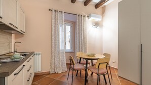 A compact kitchen with a dining area, featuring a round table, chairs, and a window with curtains. - Casa Agli Eremiti by Wonderful Italy (Palermo)