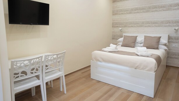 A bedroom with a bed, a TV mounted on the wall, and a chair.