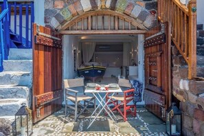 A stone archway leading to a dining area with a table set for two, a boat visible in the background, and a staircase to the left. - Gorgeous Apt in front of the Sea at Klima Milos (Klima)