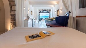 Ein Schlafzimmer mit einem Bett, einem offenen Buch, einem Boot und Meerblick durch einen Bogen.