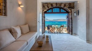 Ein Zimmer mit einem weißen Sofa, einem Holztisch und Meerblick durch einen offenen Bogen.