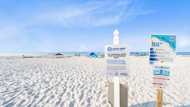 A beach with signs indicating beach safety and personal item removal policies. - Laguna Bella B5 (Gulf Shores)
