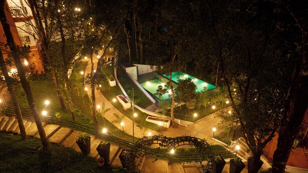 A nighttime view of a landscaped area with a swimming pool, illuminated pathways, and surrounding trees. - ERA Resort by Stride (Devikolam)