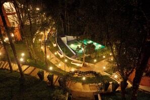 A nighttime view of a landscaped area with a swimming pool, illuminated pathways, and surrounding trees. - ERA Resort by Stride (Devikolam)