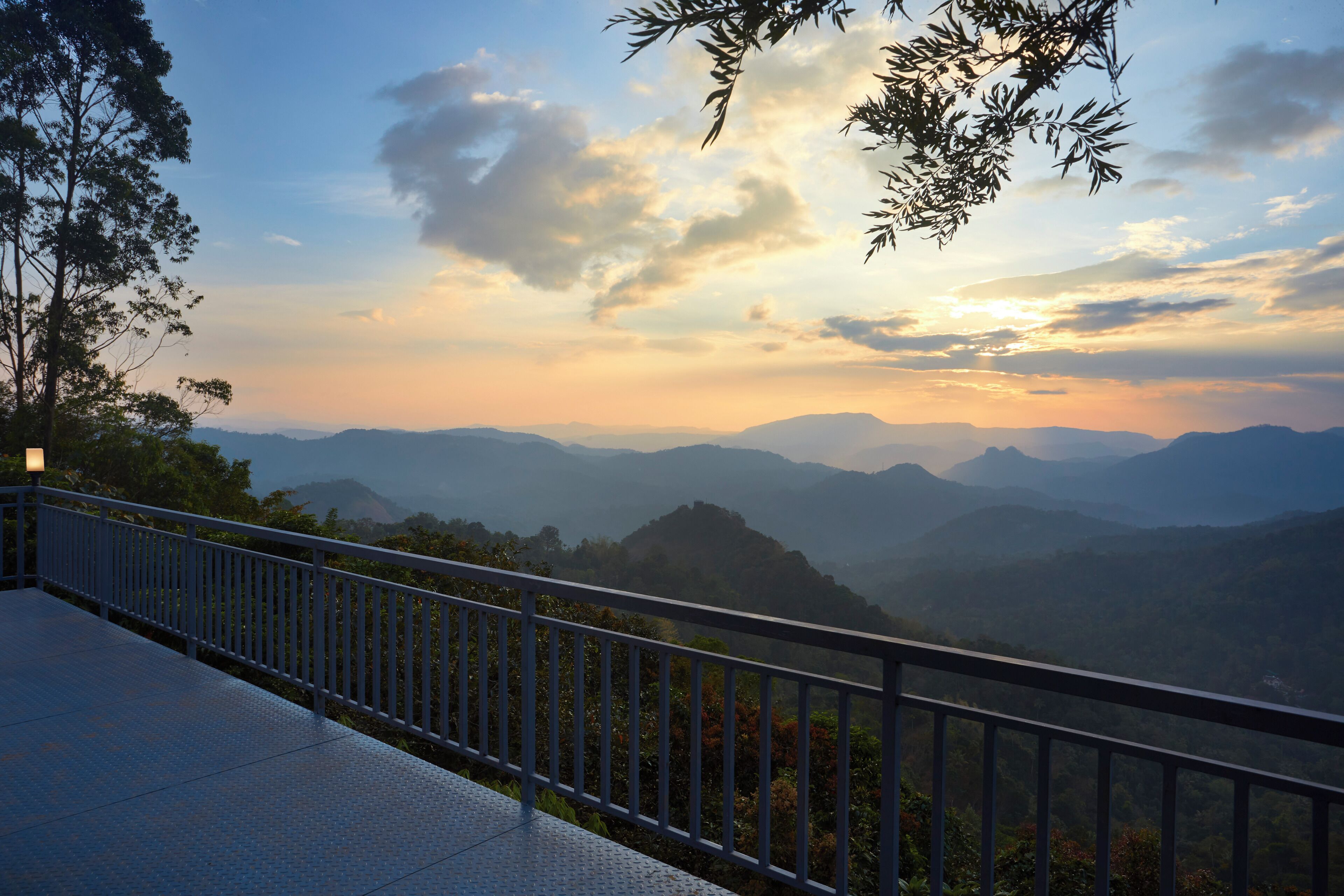 A balcony with a metal railing overlooking a mountainous landscape during sunset.