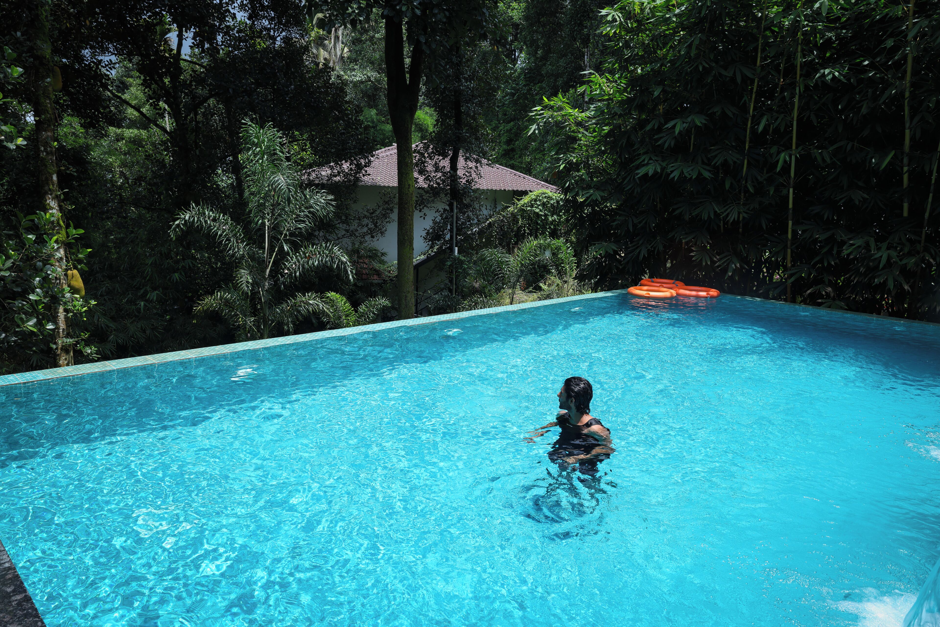 A clear blue pool surrounded by lush greenery and a building with a tiled roof.