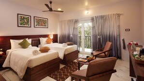 A hotel room with two beds, a sitting area, a balcony with curtains, and artwork on the walls. - ERA Resort by Stride (Devikolam)