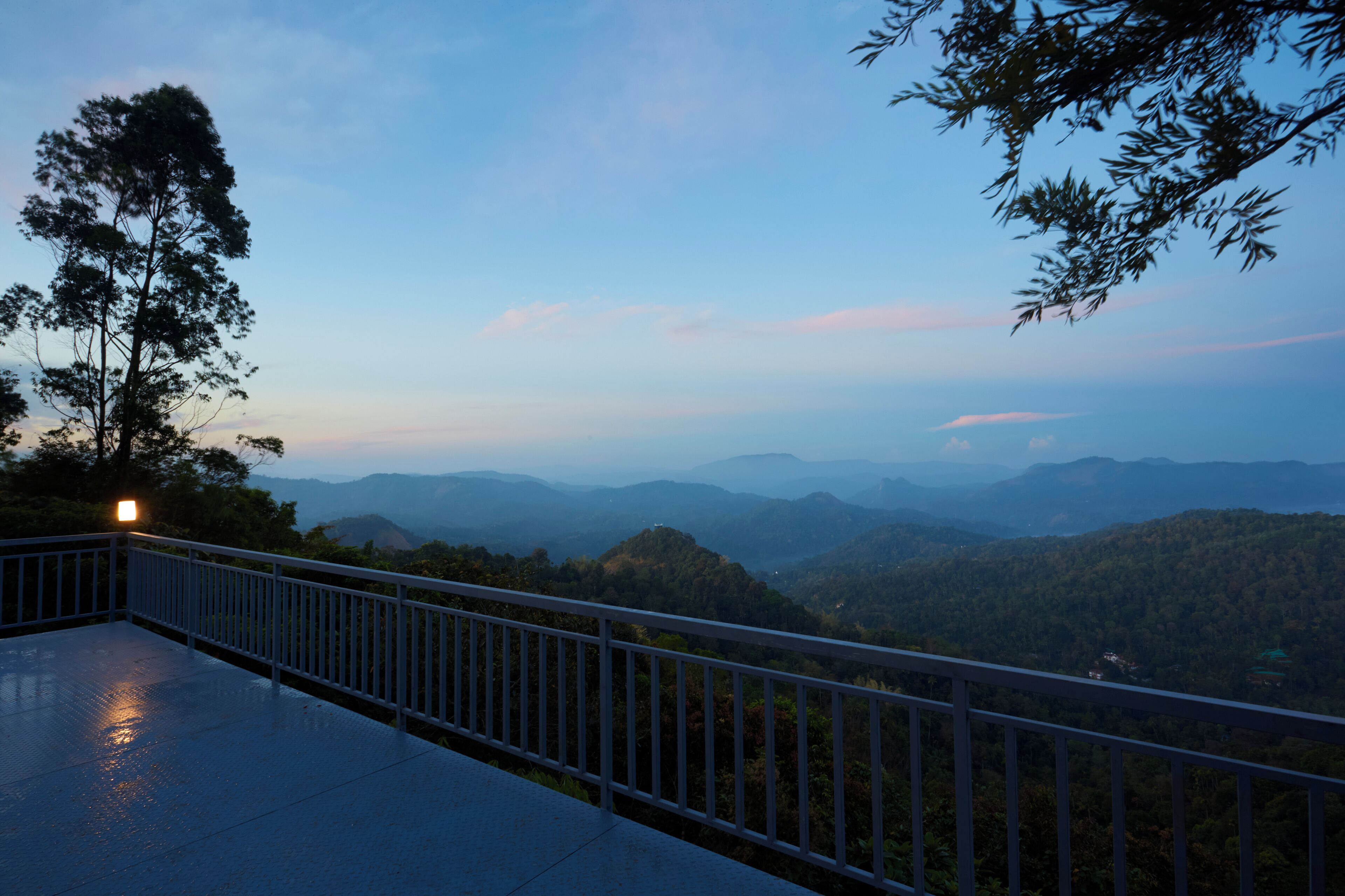 A balcony with a metal railing overlooking a mountainous landscape during twilight.