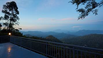 A balcony with a metal railing overlooking a mountainous landscape during twilight.