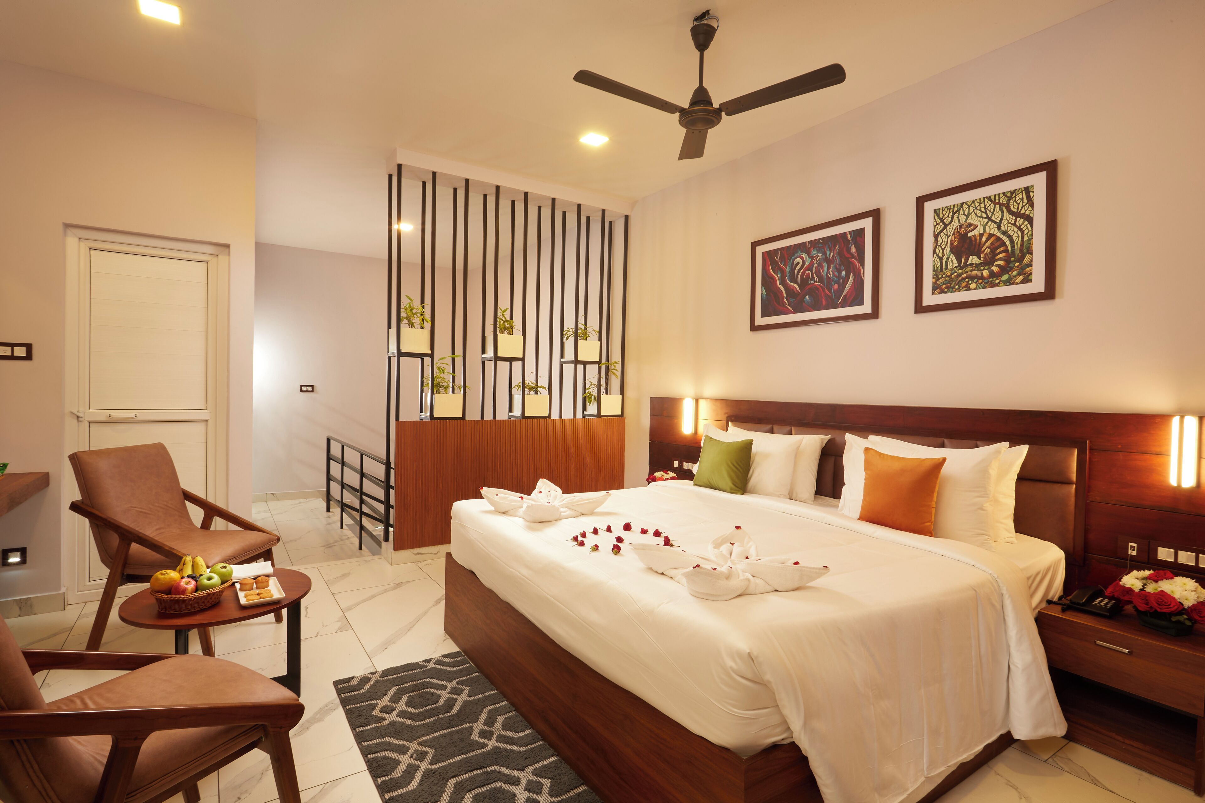 A hotel room with a large bed, a sitting area with a chair and a table, a ceiling fan, and artwork on the wall.