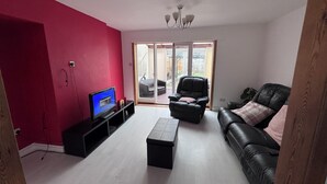 Un salon avec un mur rouge, un canapé en cuir noir, un fauteuil en cuir noir, une table basse noire et un téléviseur posé sur un meuble noir.
