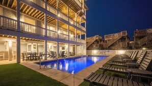 Zona de piscina con sillas de descanso y una piscina, rodeada por un edificio con varios balcones y escaleras.