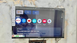 Een flatscreen televisie bevestigd aan een marmeren muur, waarop diverse streaming apps en een Google TV interface te zien is.