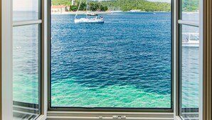 Une fenêtre donnant sur une mer calme et un voilier.
