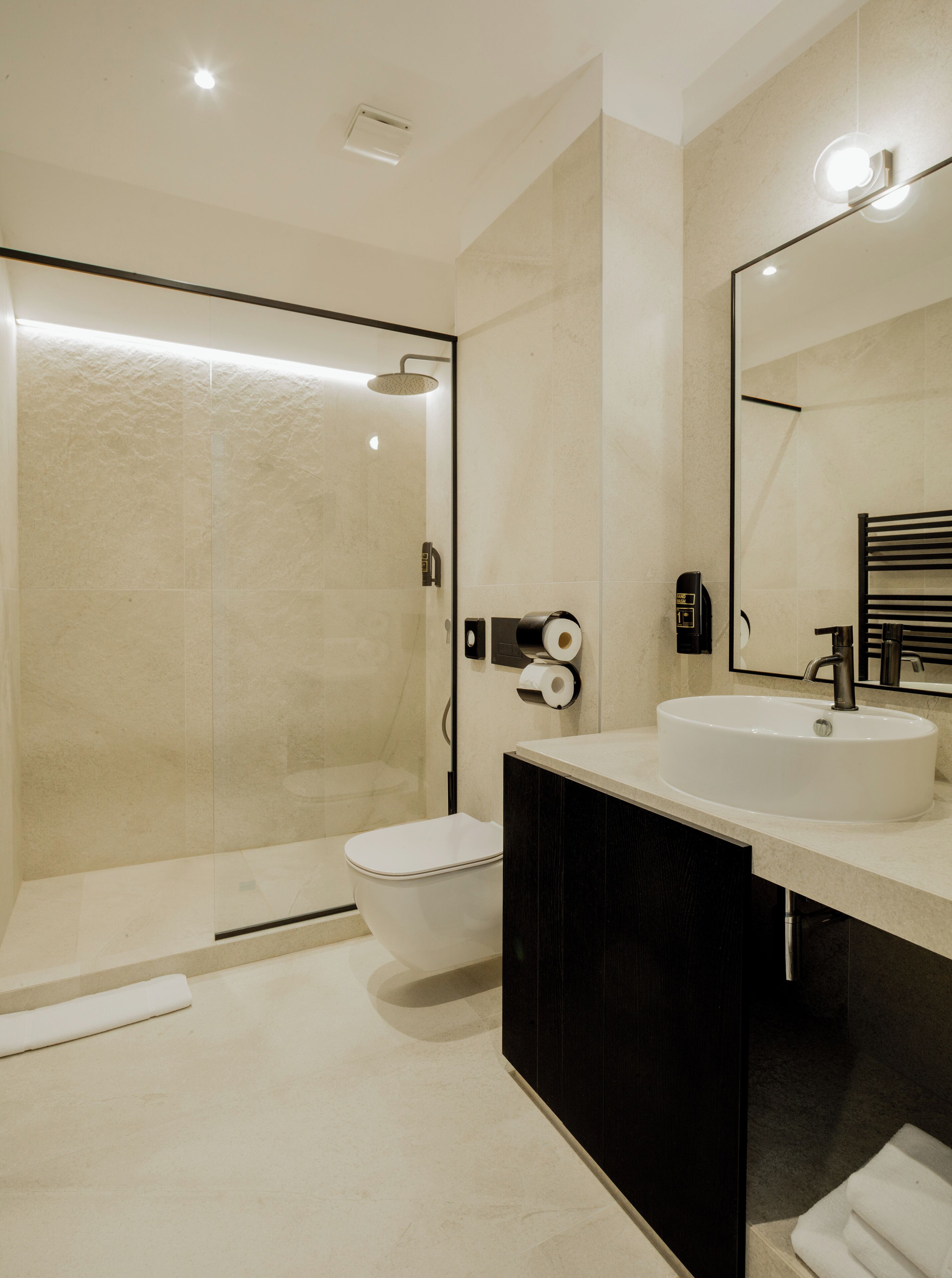Un baño moderno con ducha de vidrio, inodoro blanco y tocador negro con un espejo grande.