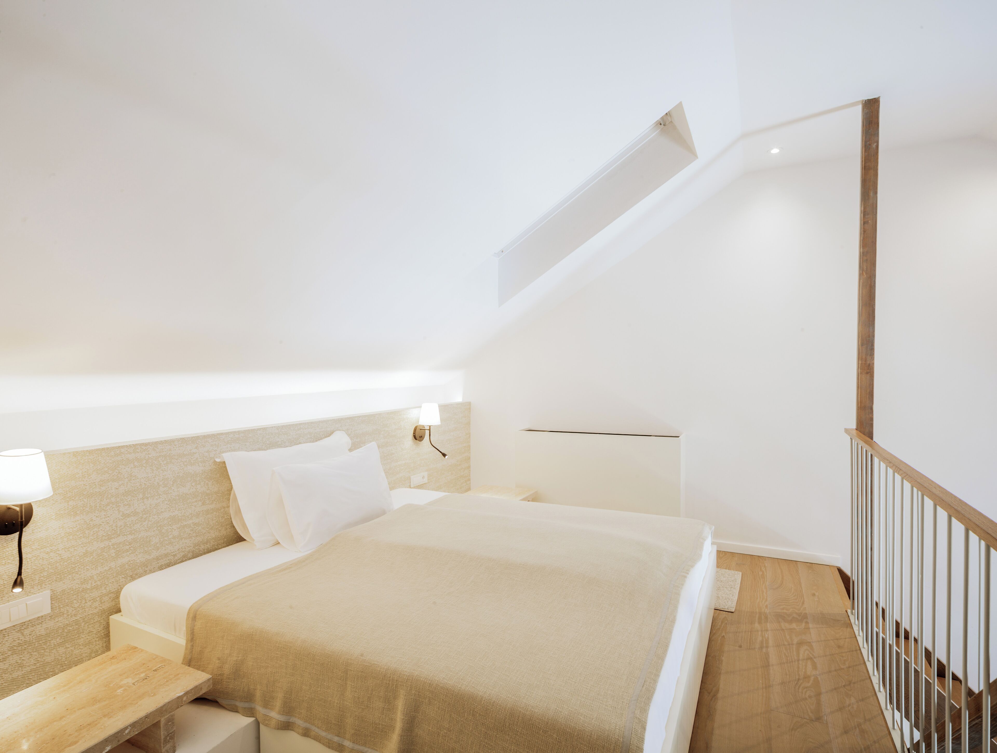 Un dormitorio con cama, mesitas de noche, cabecera, una escalera de madera y una lámpara fijada a la pared.