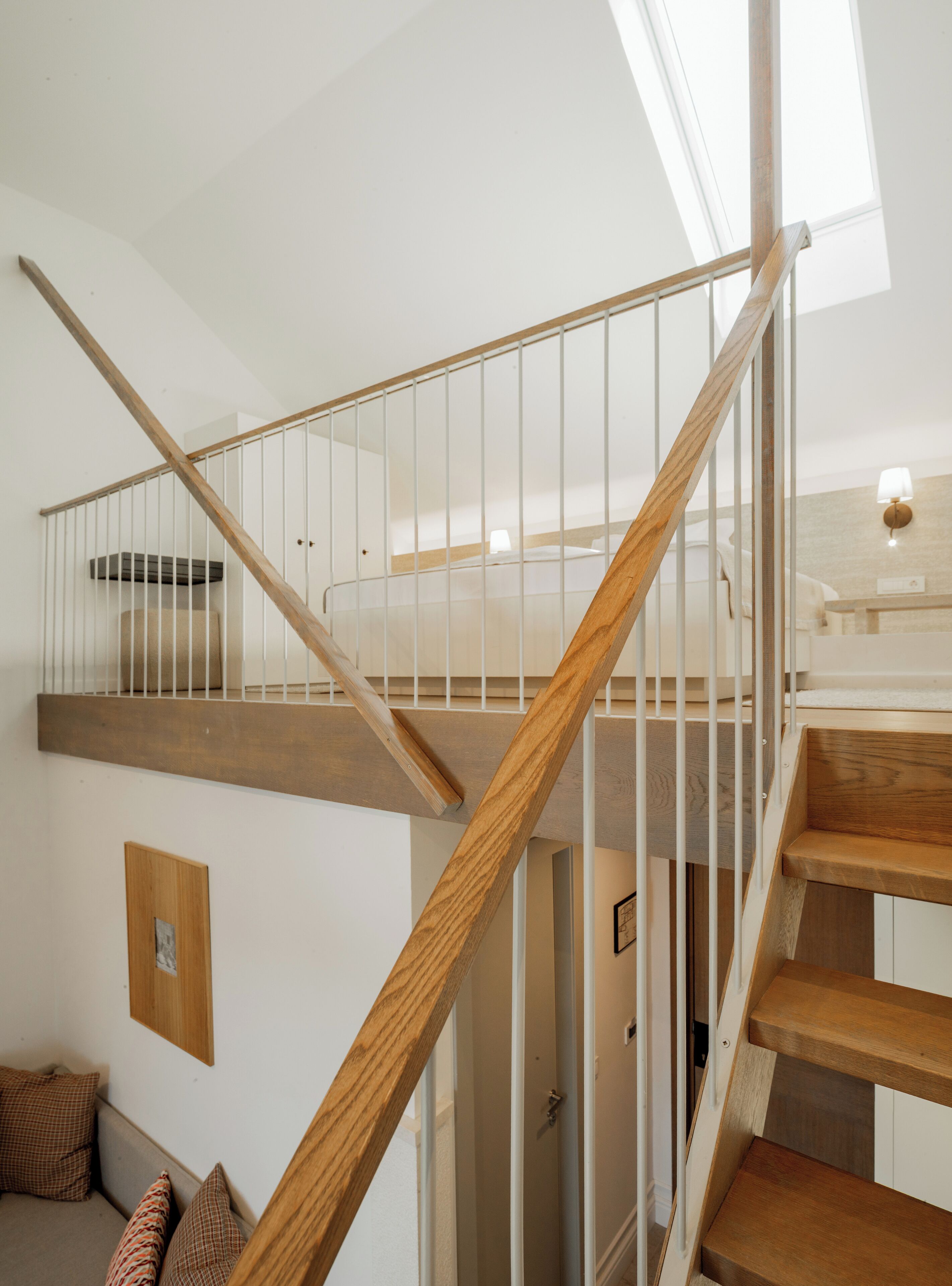 Una escalera con peldaños de madera y barandillas blancas, que conduce a un nivel superior con un tragaluz.