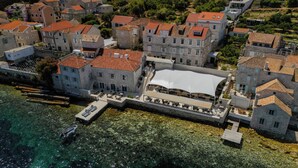 Vue aérienne d’une ville côti ère historique, avec ses bâtiments en pierre, sa promenade en bord de mer et une vaste zone couverte d’une grande tente blanche.