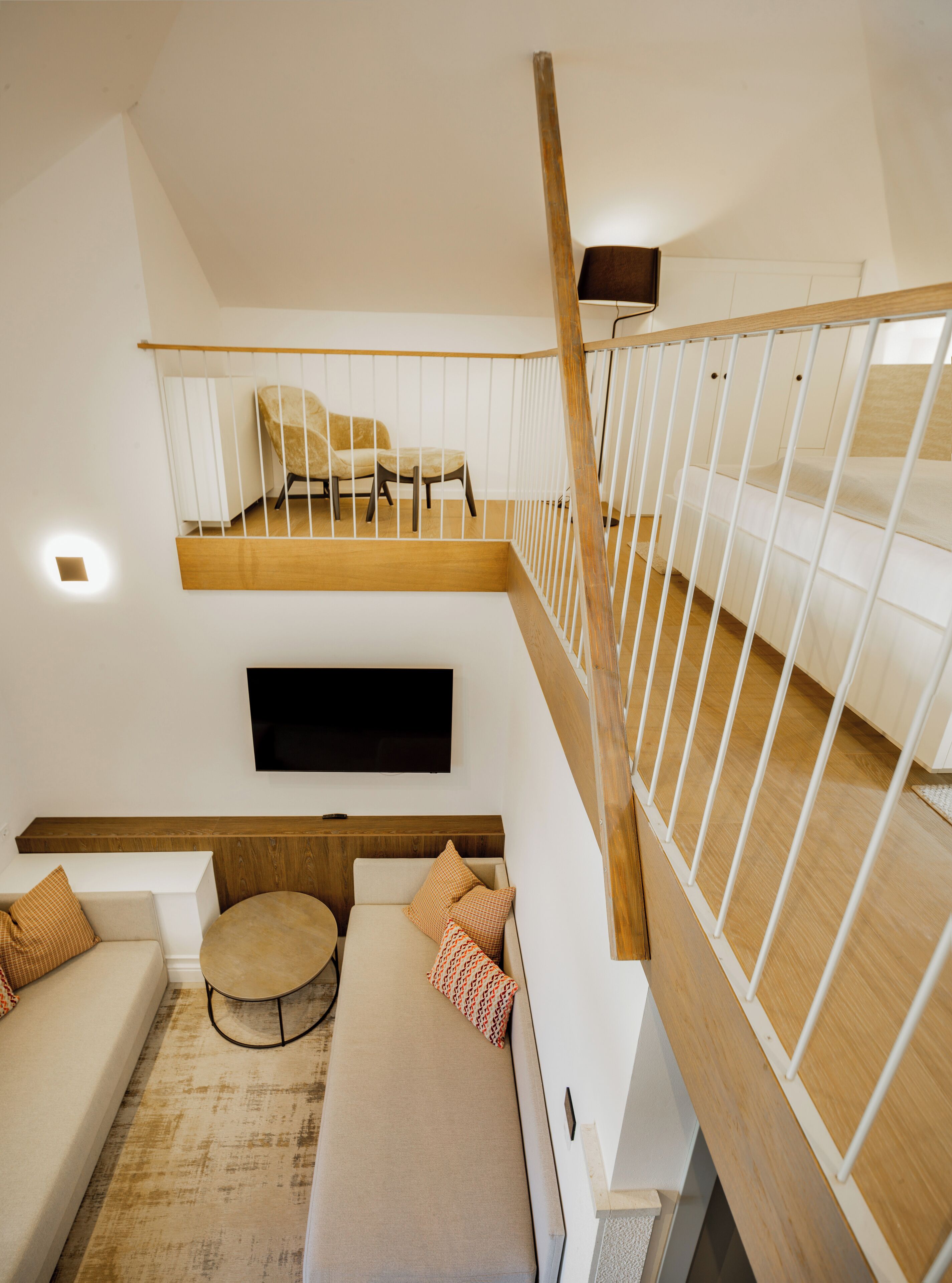 Un espacio habitable moderno estilo loft con una escalera de madera, un televisor de pantalla plana montado en la pared y una zona de estar acogedora con un sofá y una mesa de centro redonda.