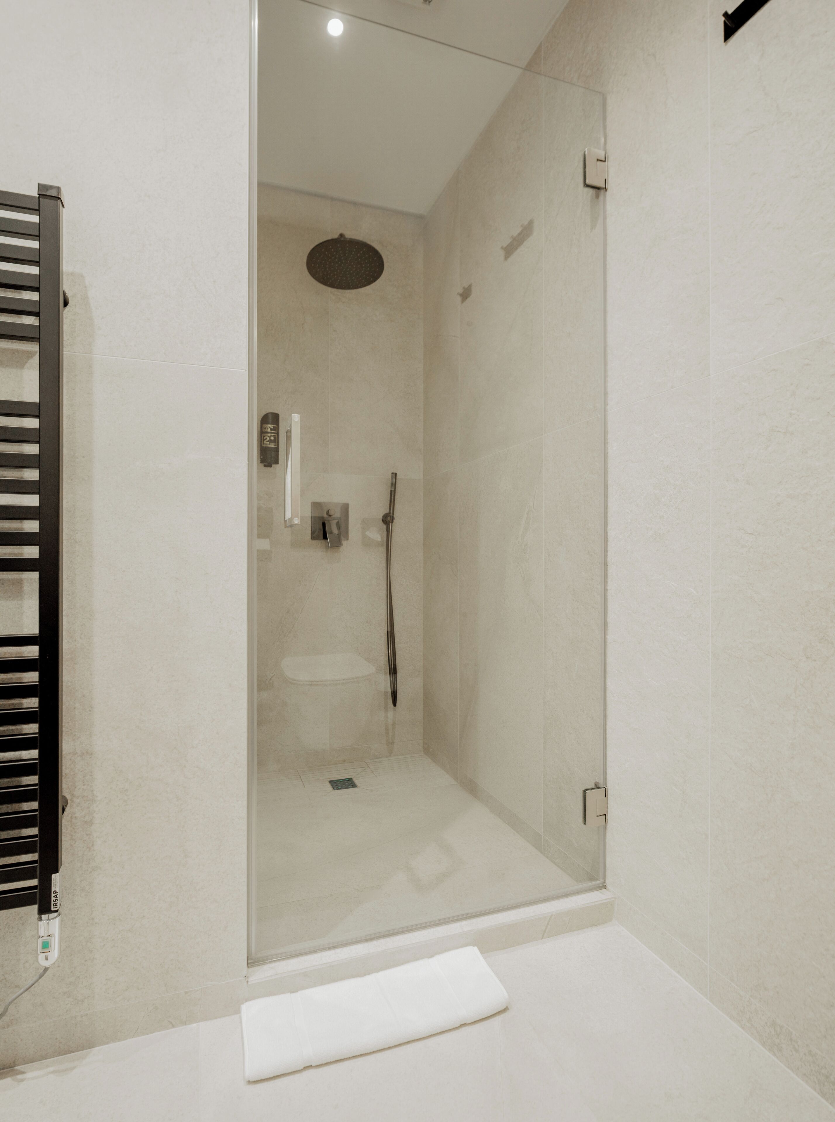 Une salle de bain moderne avec une douche à parois de verre, un lavabo blanc et une serviette sur le sol.
