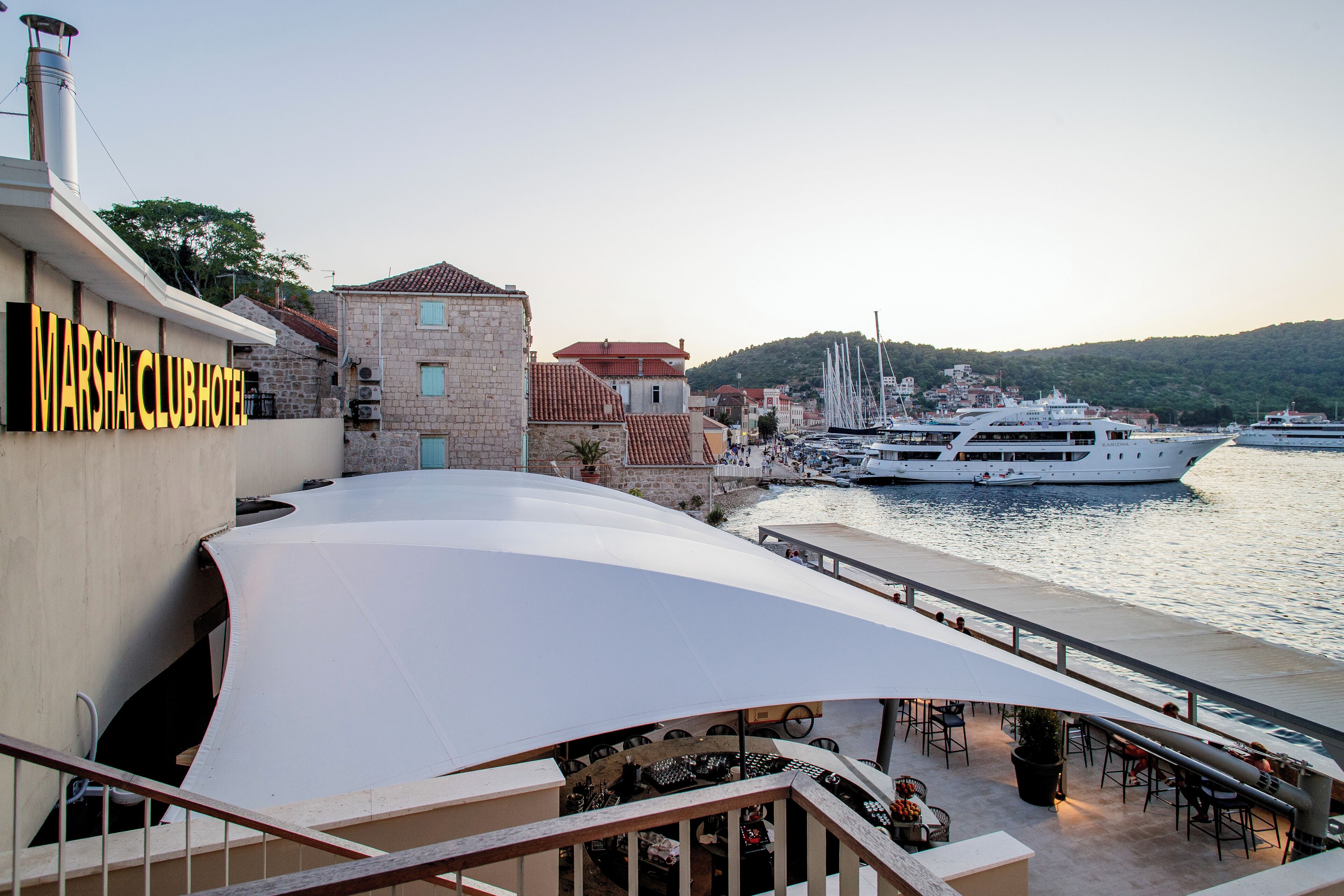 A waterfront hotel with a prominent sign, outdoor seating, and boats docked nearby.