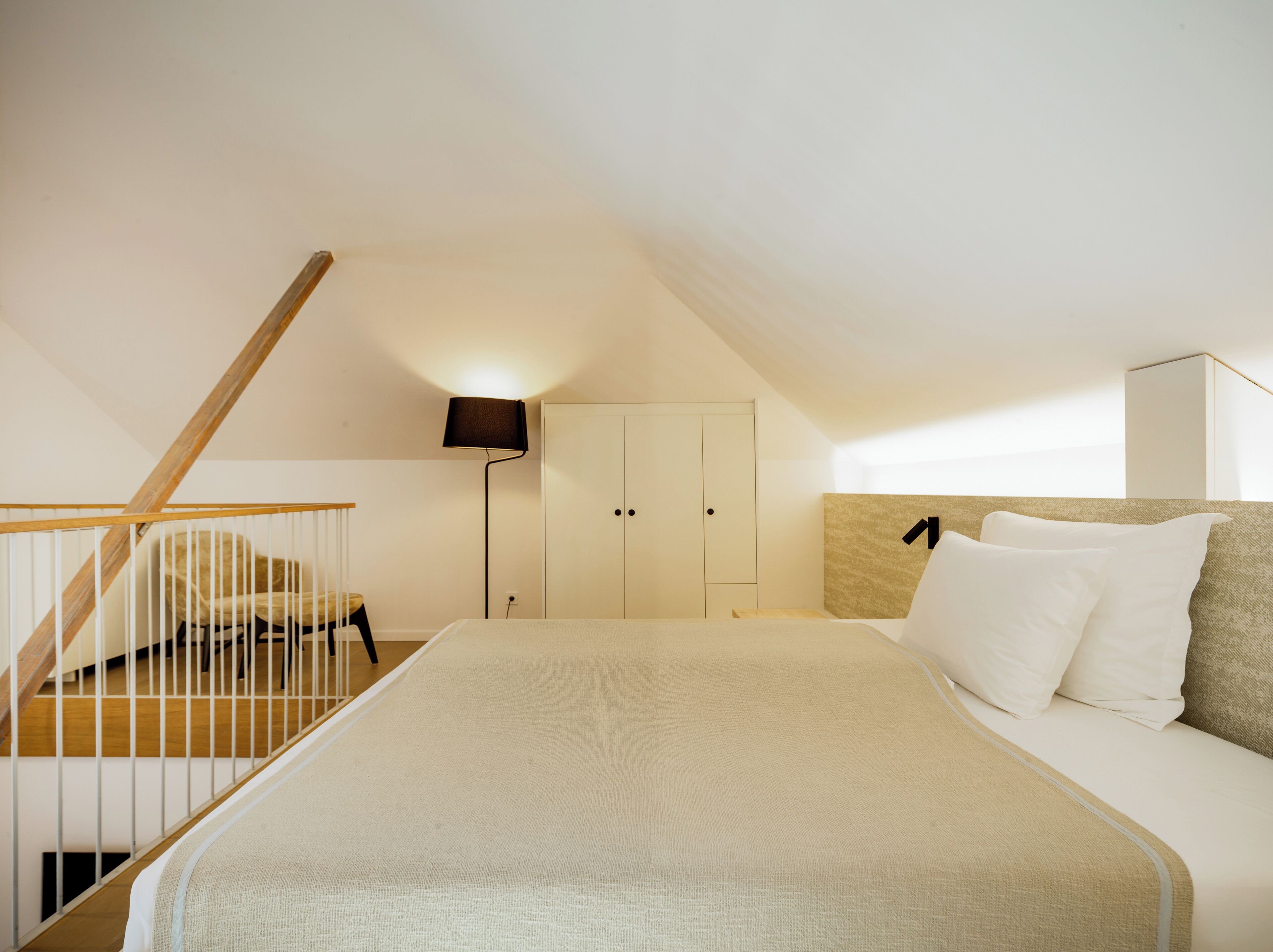 A bedroom with a bed, a nightstand, a lamp, a wardrobe, and a staircase.