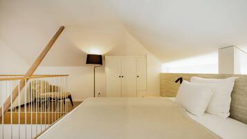 A bedroom with a bed, a nightstand, a lamp, a wardrobe, and a staircase.