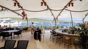 Un espace extérieur aménagé pour les repas, avec des tables et des chaises, un bar et une vue sur les bateaux qui naviguent.