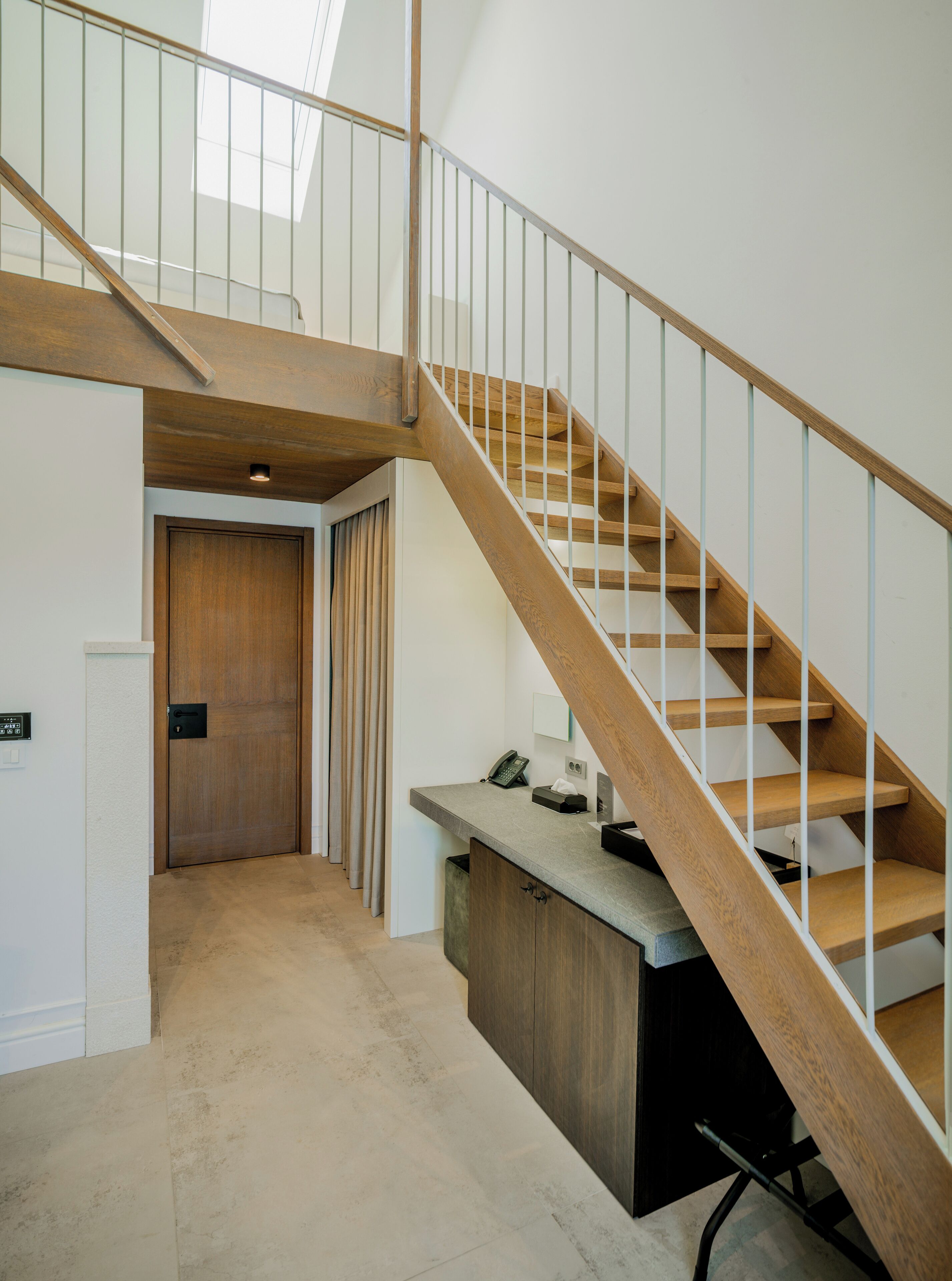 A modern interior with a wooden staircase, a desk, and a door.